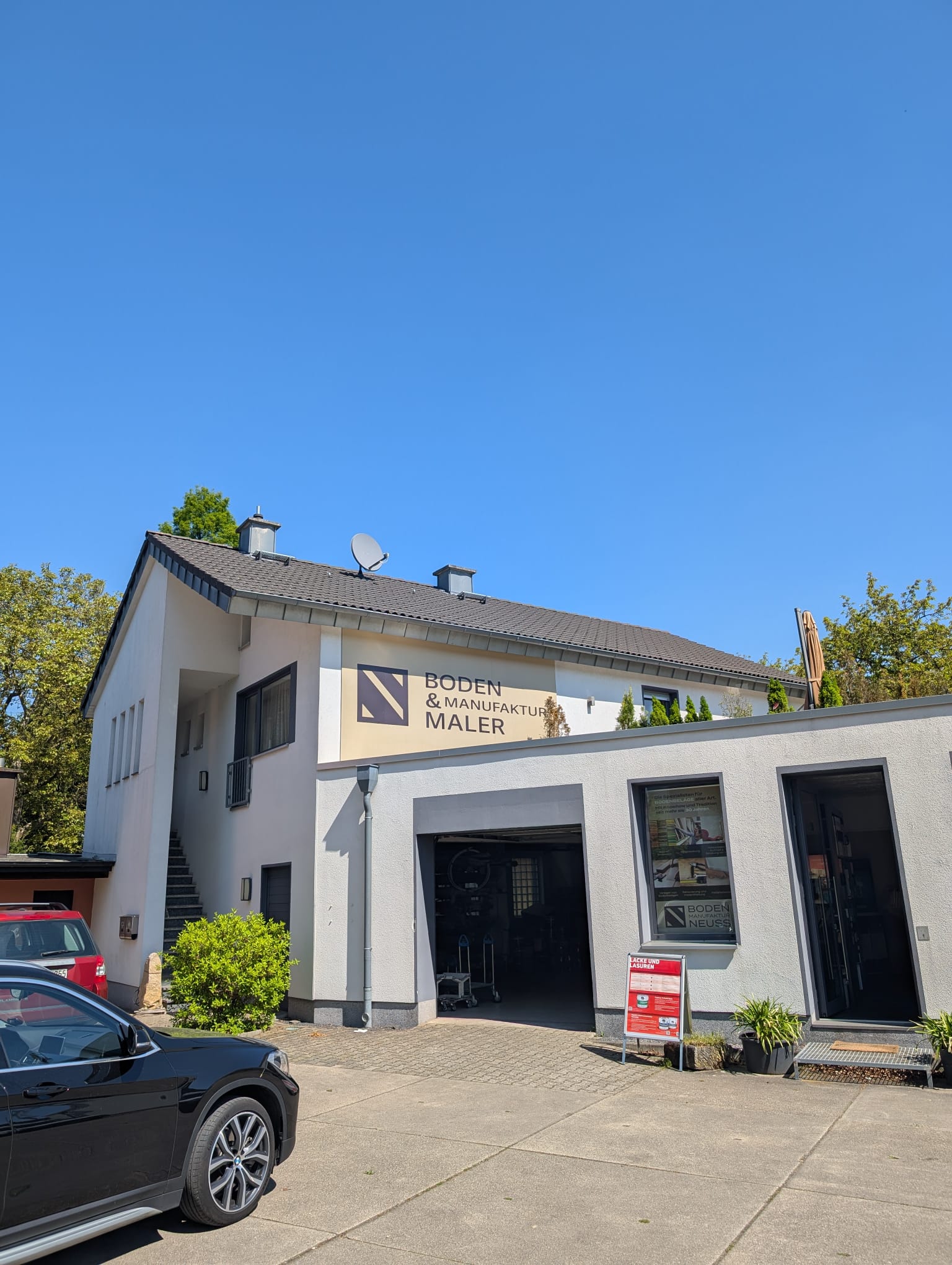 Werkstattgebaeude in Weiss mit blauem Dach und Schild unter blauem Himmel