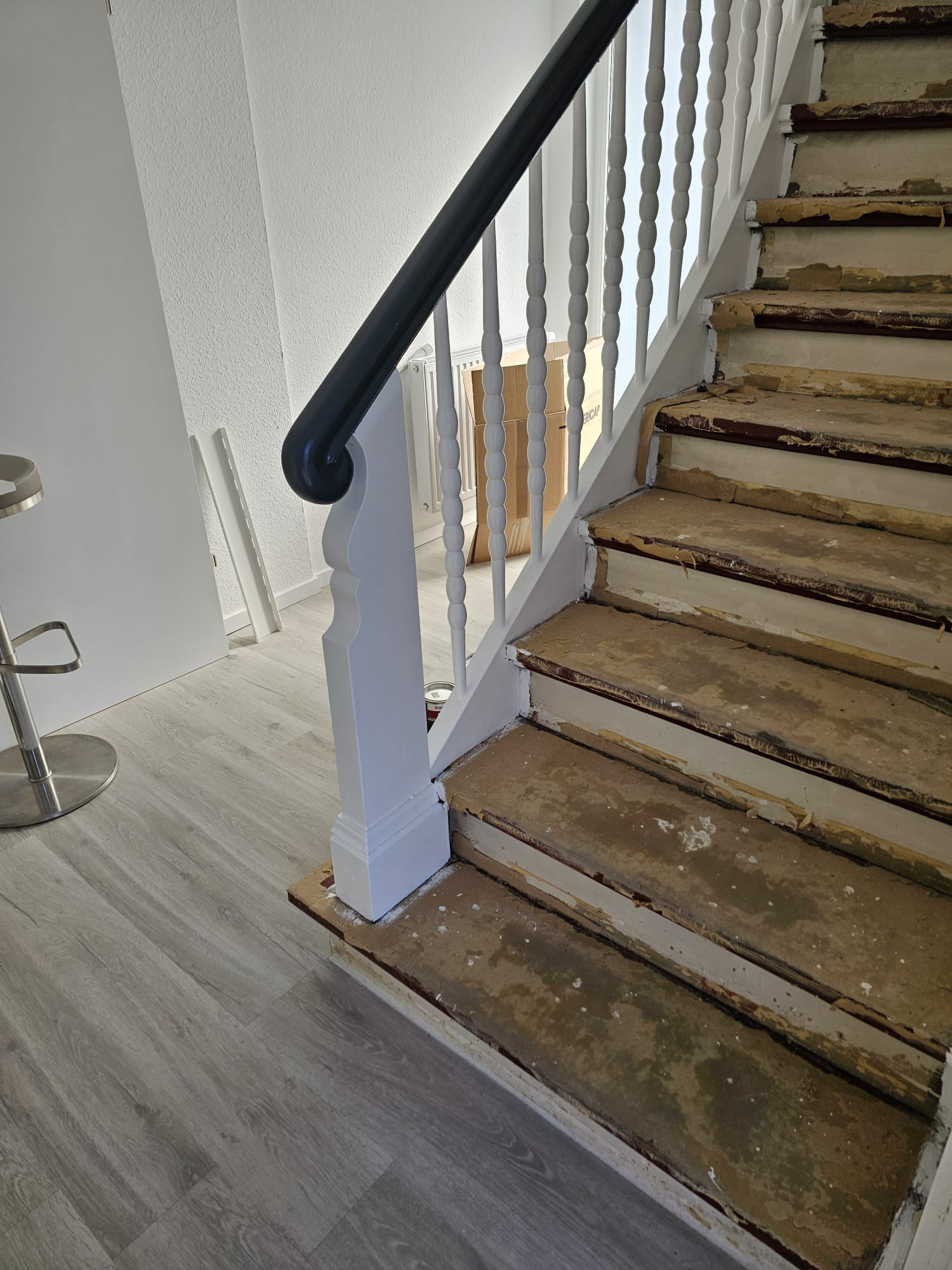 Abgenutzte braunweiße Treppe mit weißem Geländer und schwarzem Handlauf