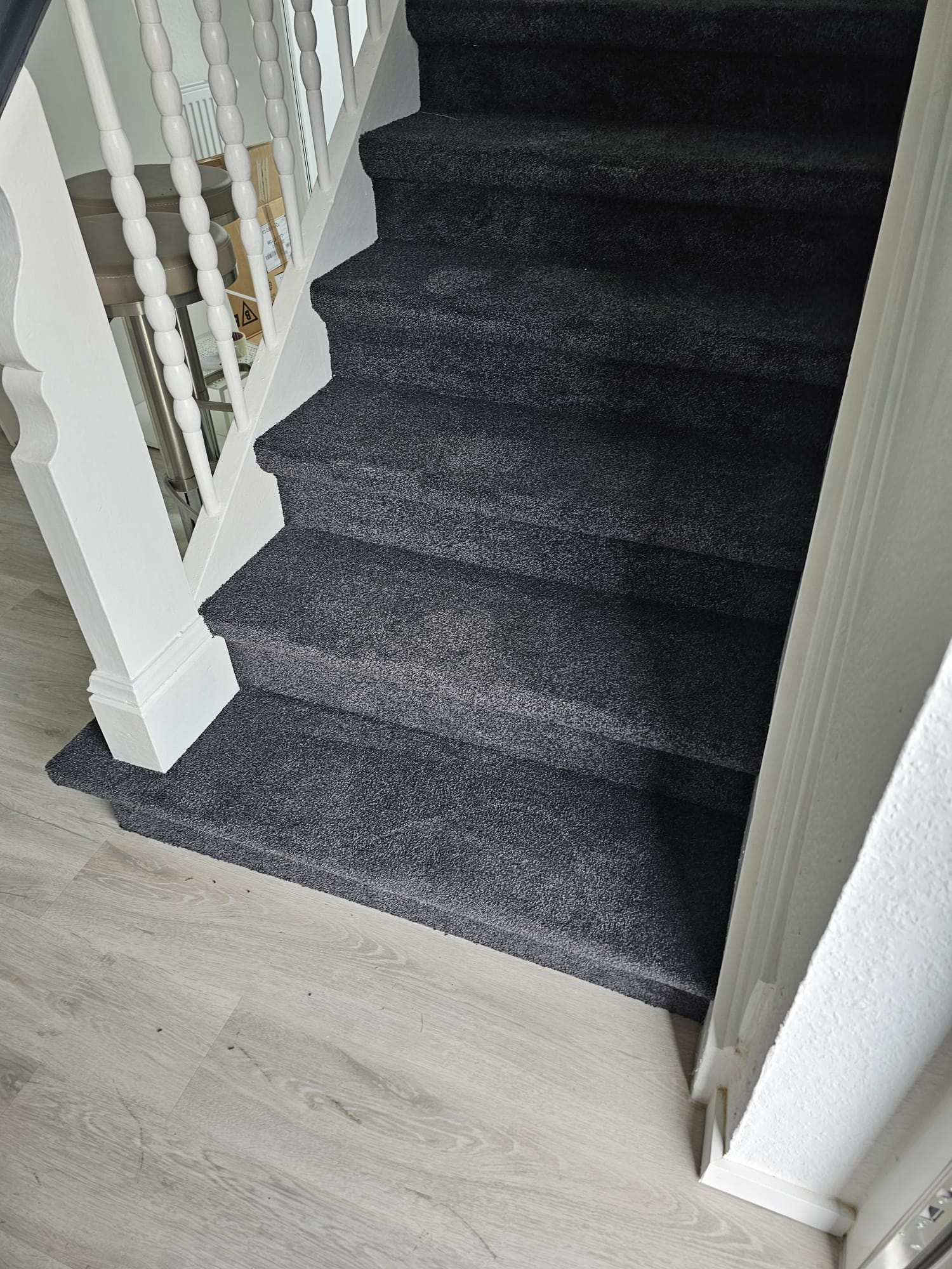 Graue Teppichtreppe mit weißen Geländerstäben und Holzfußboden am Ansatz