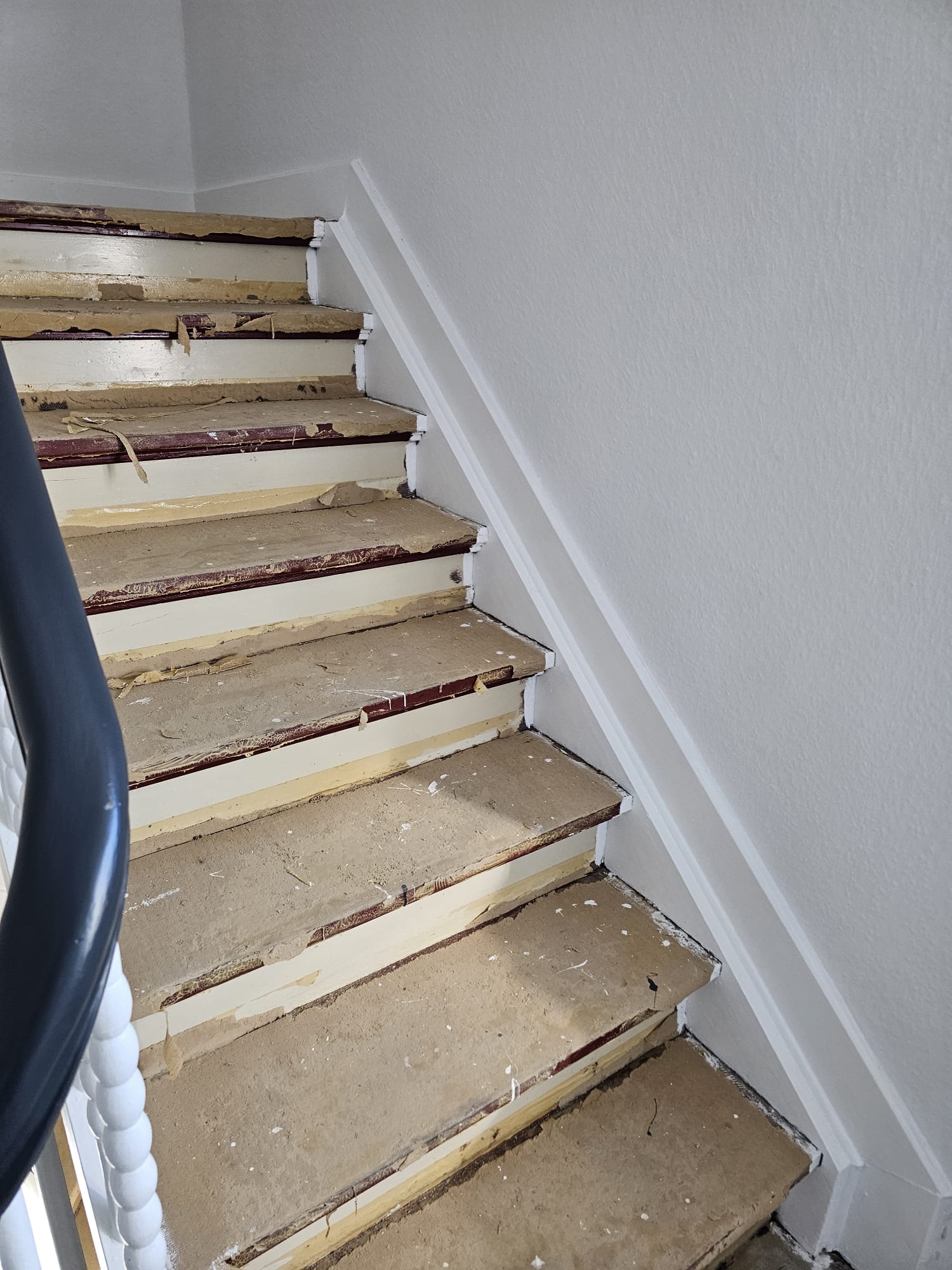 Abgenutzte beige Treppe mit beschädigten Stufen und weißem Geländer links