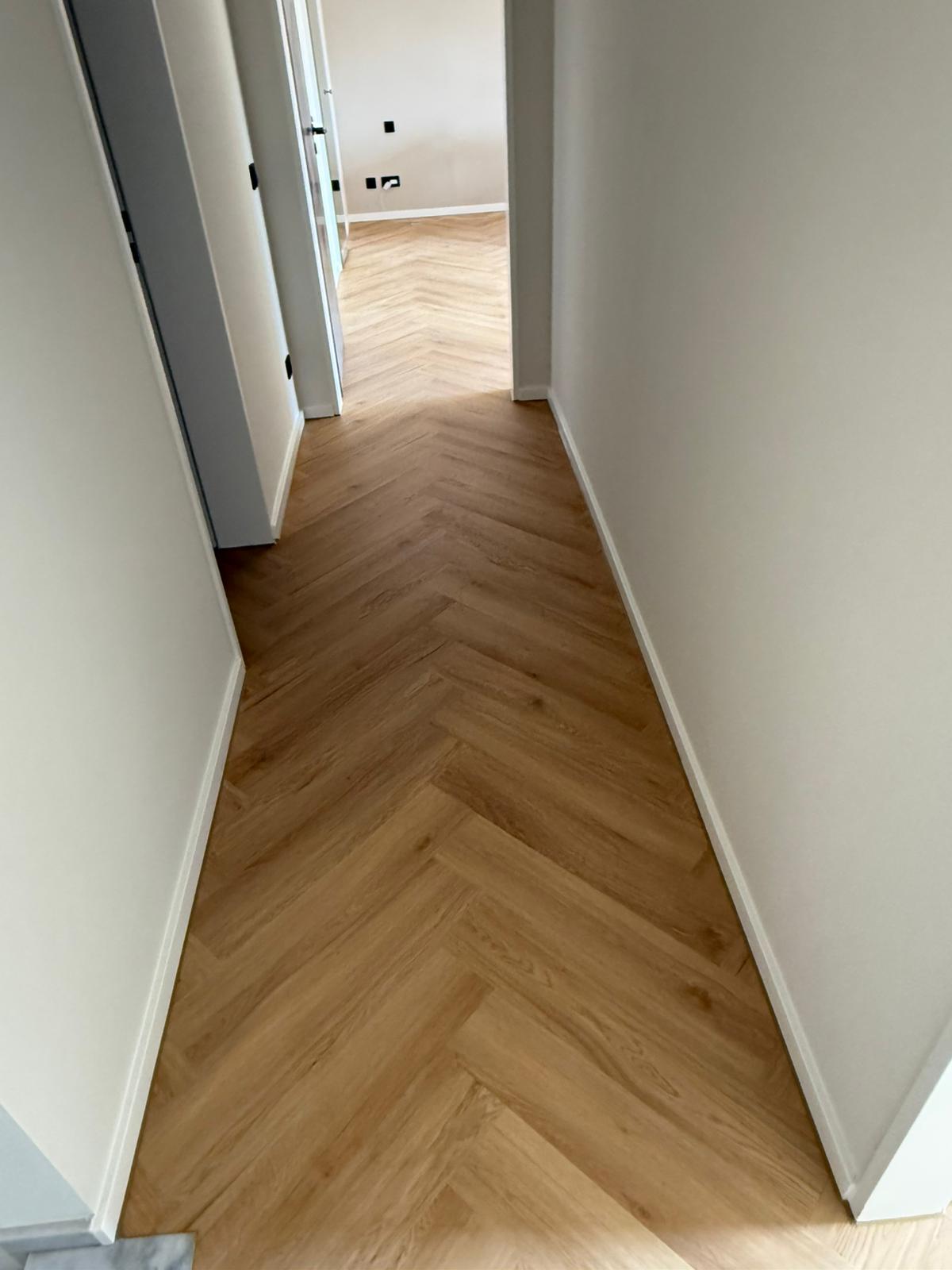 Heller Flur mit weißer Wand und braunem Fischgraetparkett, Tueren offen