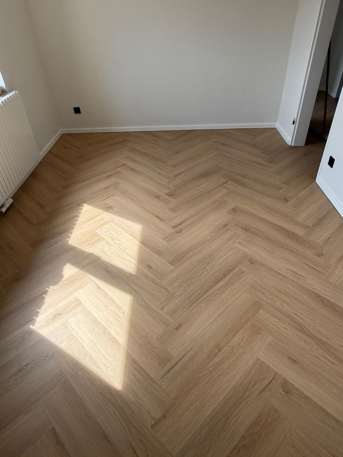 Leerer Raum mit hellem Fischgraetparkett und Sonnenlichtfleck in Beige