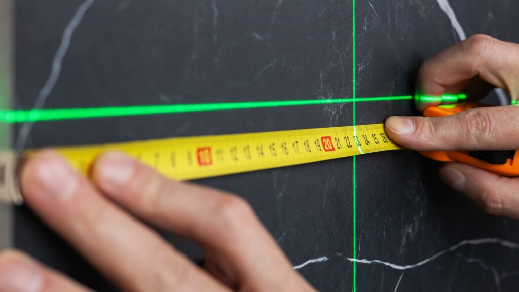 die Hände eines Arbeiters, der die Breite einer Tischplatte mit einem Maßband und einem Laser misst